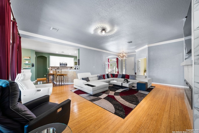 living room with arched walkways, a textured ceiling, visible vents, light wood finished floors, and crown molding