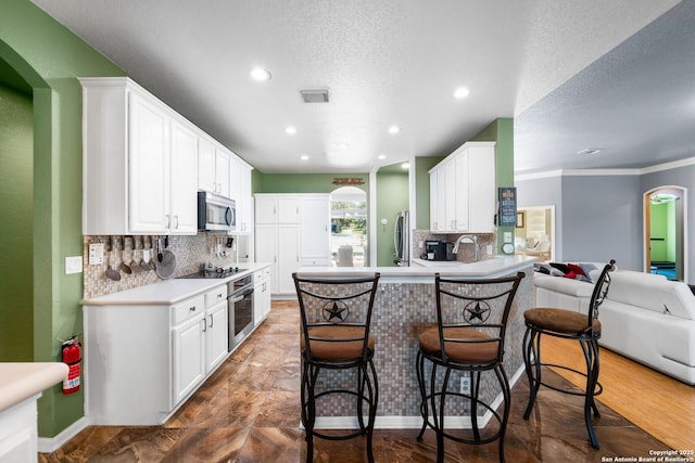 kitchen with open floor plan, a peninsula, stainless steel appliances, light countertops, and white cabinetry