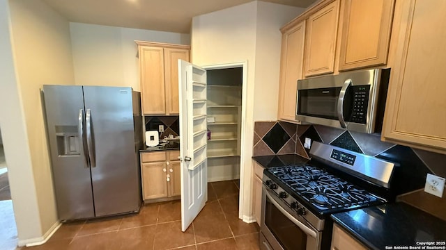 kitchen featuring dark tile patterned flooring, backsplash, light brown cabinets, and appliances with stainless steel finishes