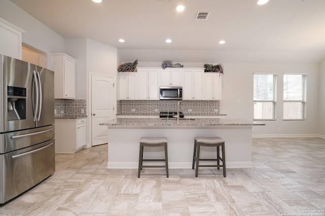 kitchen featuring white cabinetry, appliances with stainless steel finishes, an island with sink, and light stone counters