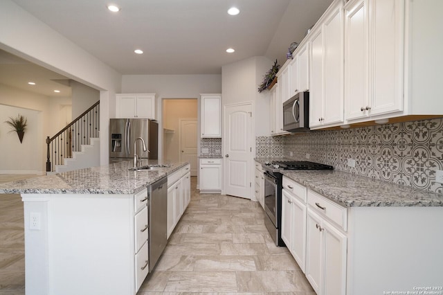 kitchen with an island with sink, appliances with stainless steel finishes, white cabinets, and light stone counters