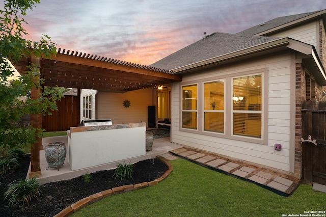 back house at dusk with exterior kitchen, a yard, a pergola, and a patio area