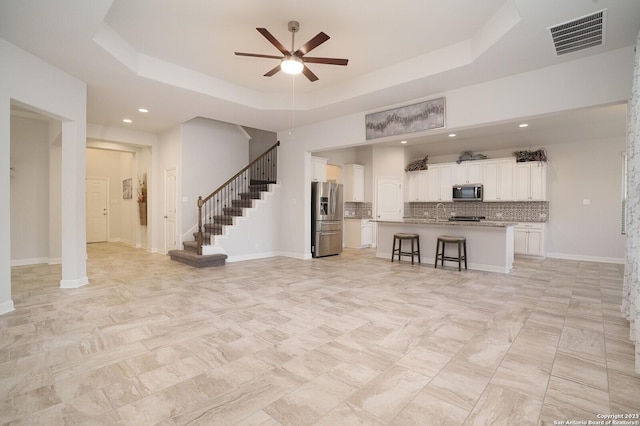 unfurnished living room with a raised ceiling and ceiling fan