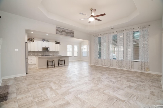 unfurnished living room featuring a raised ceiling and ceiling fan