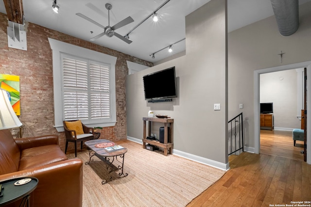 living room with hardwood / wood-style flooring, ceiling fan, brick wall, and rail lighting