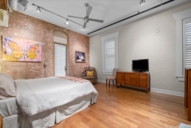 bedroom with track lighting, brick wall, and light wood-type flooring