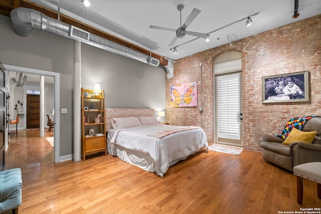 bedroom featuring a towering ceiling, brick wall, and light hardwood / wood-style flooring