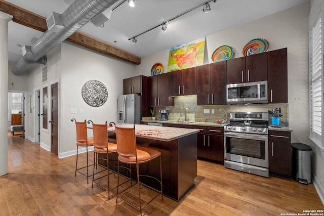 kitchen with sink, appliances with stainless steel finishes, a center island, dark brown cabinetry, and a kitchen bar