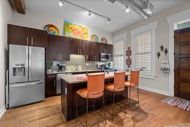 kitchen with a breakfast bar, light hardwood / wood-style flooring, a kitchen island, stainless steel appliances, and backsplash