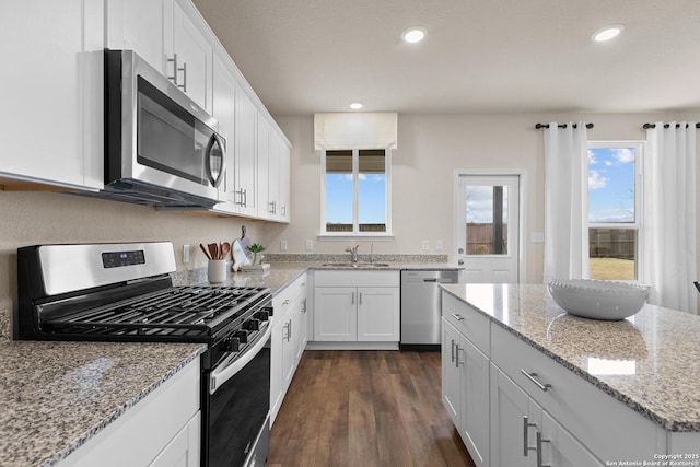 kitchen featuring appliances with stainless steel finishes, dark hardwood / wood-style floors, white cabinetry, sink, and light stone countertops