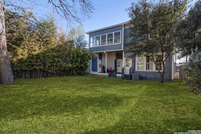 rear view of house with central AC unit and a lawn