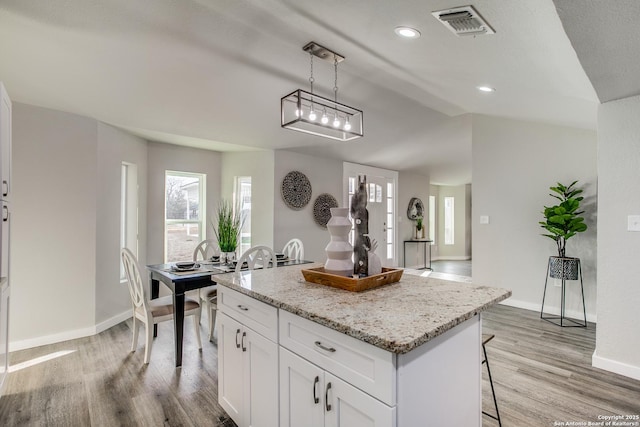 kitchen featuring a kitchen breakfast bar, a center island, light stone countertops, white cabinets, and decorative light fixtures