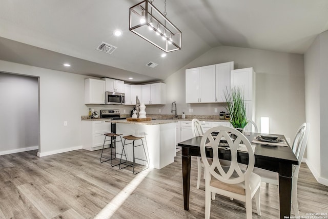 kitchen featuring appliances with stainless steel finishes, white cabinetry, hanging light fixtures, light hardwood / wood-style floors, and a kitchen island