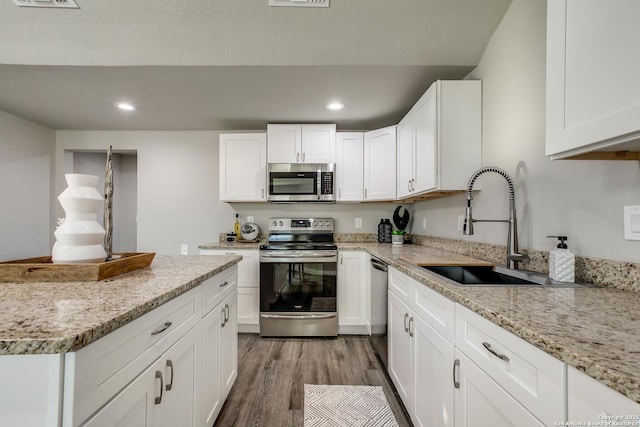 kitchen featuring sink, light stone counters, appliances with stainless steel finishes, hardwood / wood-style floors, and white cabinets