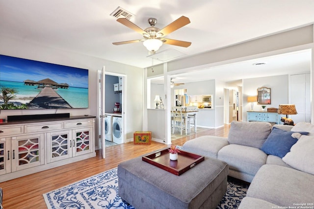 living room featuring washer and clothes dryer, ceiling fan, and light wood-type flooring