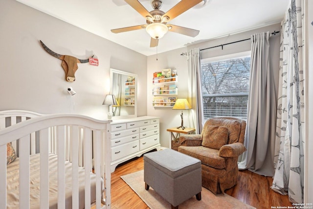 bedroom featuring light hardwood / wood-style flooring, a nursery area, and ceiling fan