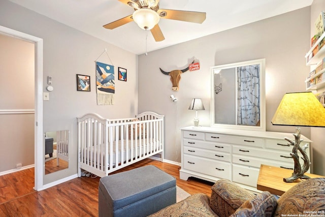 bedroom featuring a crib, dark hardwood / wood-style floors, and ceiling fan