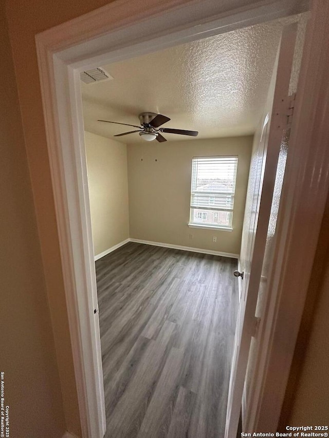 empty room featuring dark wood-type flooring, ceiling fan, and a textured ceiling