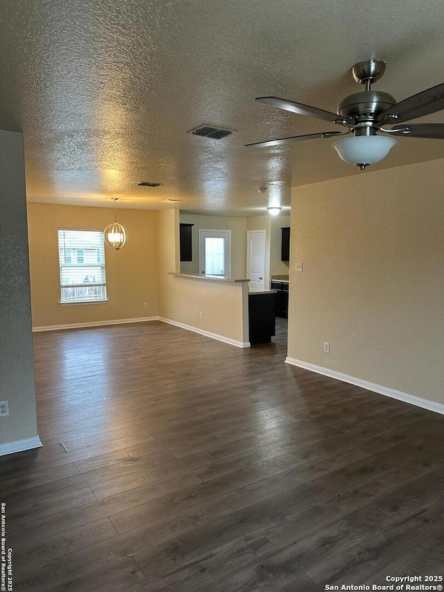 unfurnished living room featuring a wealth of natural light, dark wood-type flooring, a textured ceiling, and ceiling fan with notable chandelier