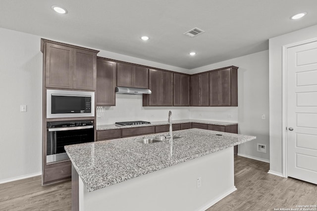 2439 Tinkerton, San Antonio, TX 78245 - kitchen featuring appliances with stainless steel finishes, a sink, light wood finished floors, dark brown cabinets, and light stone counters