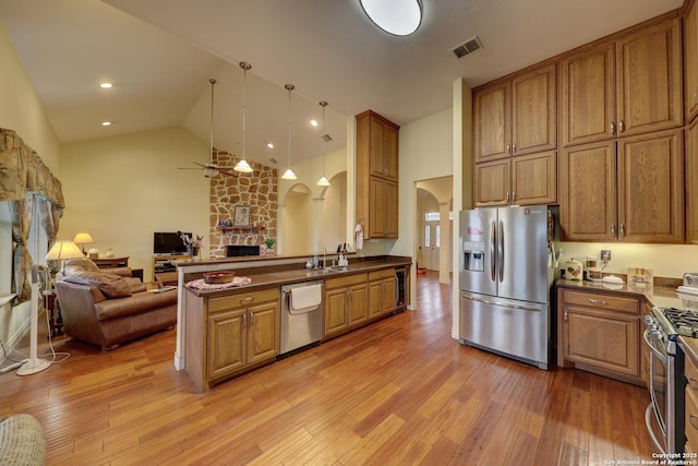 kitchen featuring light wood-type flooring, appliances with stainless steel finishes, kitchen peninsula, pendant lighting, and a fireplace