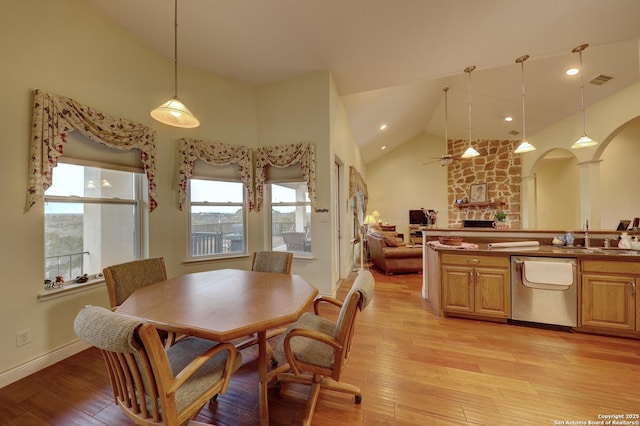 dining space featuring sink, ceiling fan, high vaulted ceiling, light hardwood / wood-style floors, and a stone fireplace