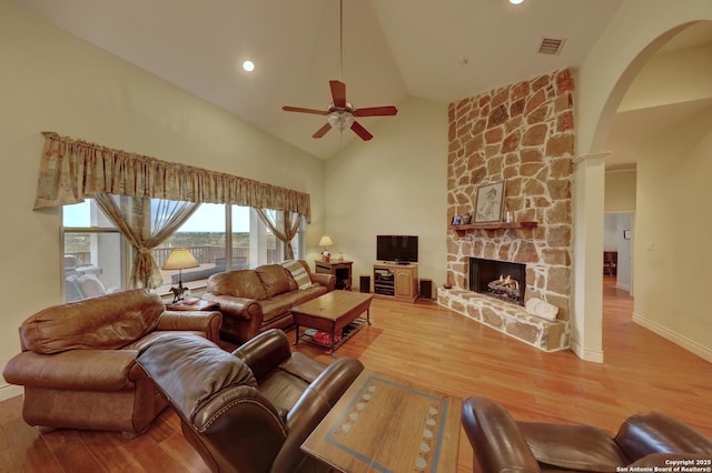 living room with ceiling fan, a stone fireplace, high vaulted ceiling, and light hardwood / wood-style floors