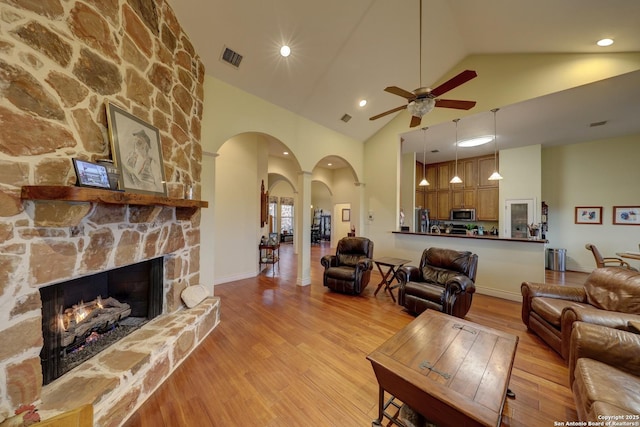 living room with high vaulted ceiling, a stone fireplace, light hardwood / wood-style floors, and ceiling fan