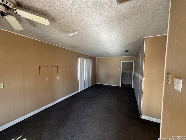 spare room with dark carpet, a textured ceiling, wooden walls, and ceiling fan