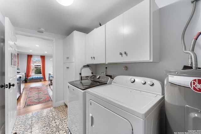 clothes washing area with cabinets, washing machine and clothes dryer, and water heater