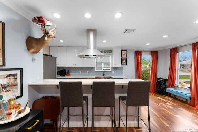 kitchen featuring a breakfast bar, white cabinetry, stainless steel refrigerator, island exhaust hood, and backsplash