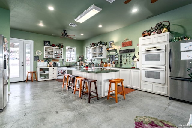 kitchen with a kitchen island, white cabinets, a kitchen bar, stainless steel fridge, and white double oven