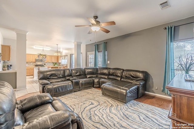 living room with light wood-type flooring, ceiling fan, and ornate columns