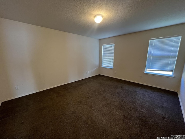 unfurnished room with dark colored carpet and a textured ceiling