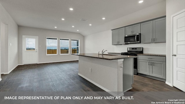 kitchen with dark stone counters, dark hardwood / wood-style flooring, gray cabinets, an island with sink, and stainless steel appliances