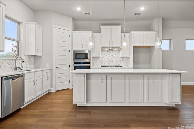 kitchen featuring a kitchen island, sink, white cabinets, hanging light fixtures, and stainless steel appliances