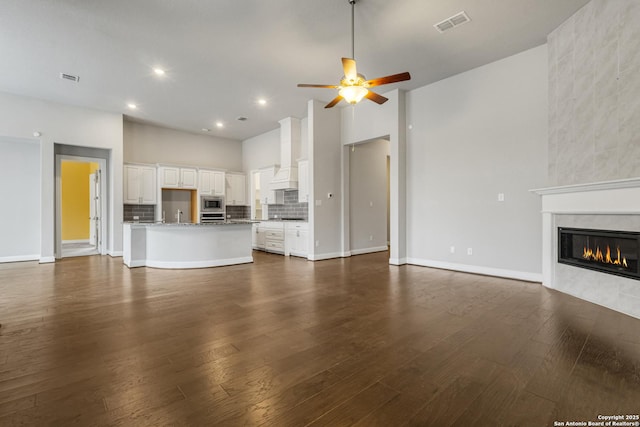 unfurnished living room with sink, dark hardwood / wood-style floors, a towering ceiling, ceiling fan, and a tiled fireplace