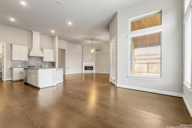 kitchen with premium range hood, dark hardwood / wood-style floors, white cabinetry, backsplash, and a center island with sink