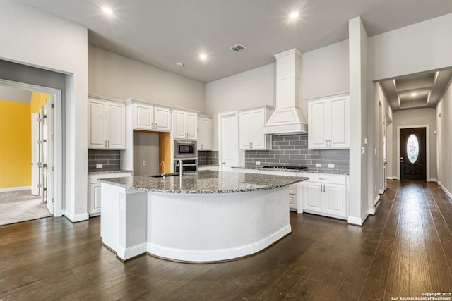 kitchen with stainless steel appliances, white cabinetry, a kitchen island with sink, and dark stone countertops