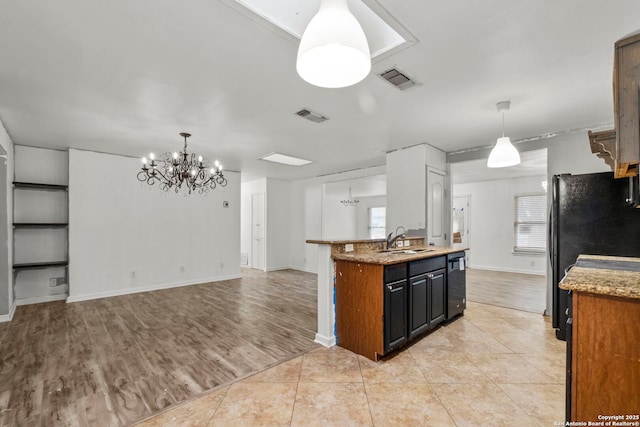 kitchen featuring sink, light stone counters, black fridge, light tile patterned floors, and pendant lighting