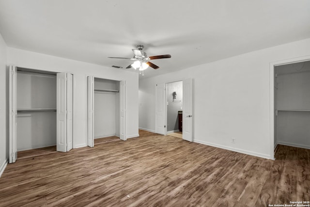 unfurnished bedroom featuring ceiling fan, hardwood / wood-style floors, and two closets