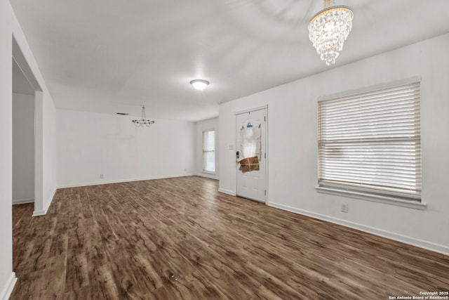 unfurnished living room featuring an inviting chandelier and dark hardwood / wood-style flooring