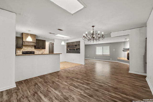 kitchen featuring stone counters, an inviting chandelier, dark brown cabinets, dark hardwood / wood-style floors, and decorative backsplash