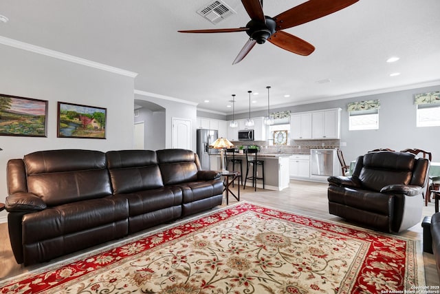 living area with visible vents, arched walkways, ceiling fan, ornamental molding, and light wood-type flooring