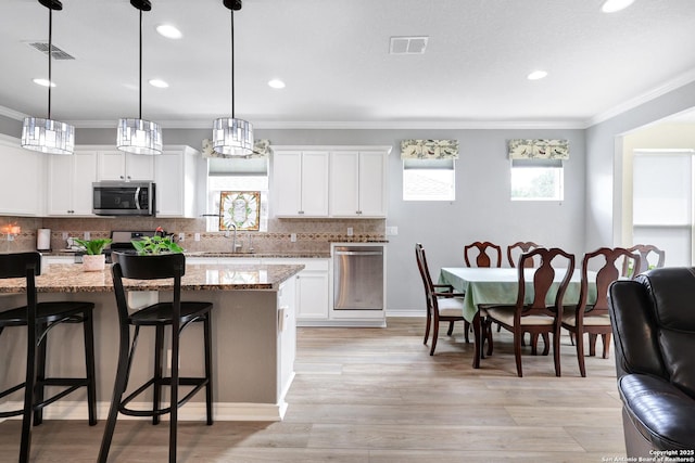 kitchen with visible vents, decorative backsplash, appliances with stainless steel finishes, a sink, and a kitchen breakfast bar