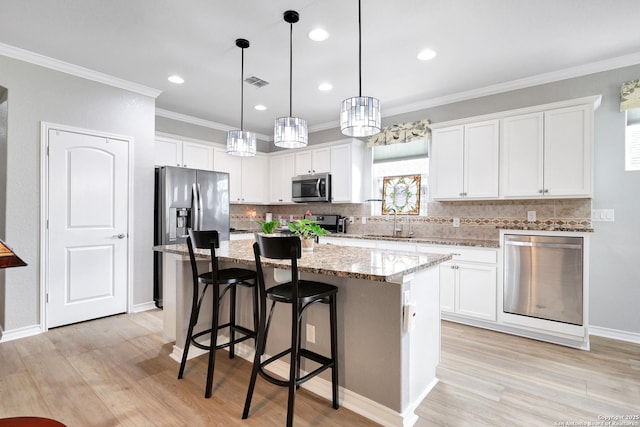 kitchen featuring stainless steel appliances, a kitchen island, visible vents, white cabinetry, and a kitchen bar