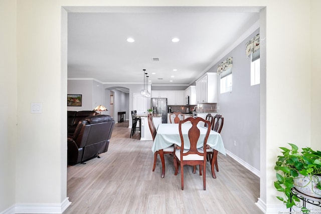 dining area featuring arched walkways, light wood-style flooring, visible vents, baseboards, and crown molding