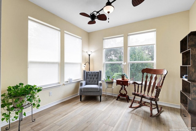 living area with wood finished floors, a ceiling fan, and baseboards