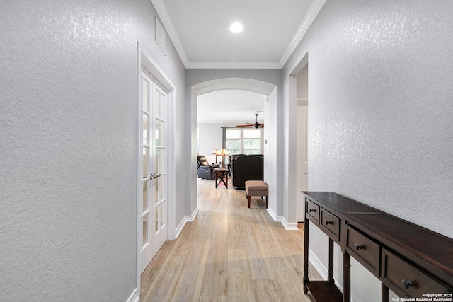 hall with light wood finished floors, arched walkways, crown molding, and a textured wall