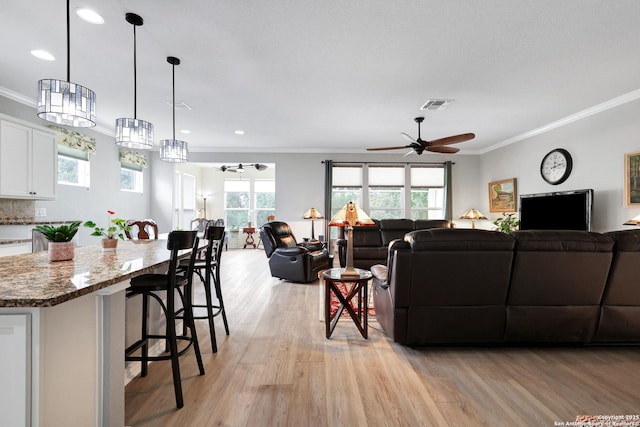 living area featuring light wood-style floors, ceiling fan, visible vents, and crown molding